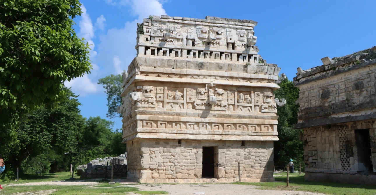 Estructura maya tallada con detalles arquitectónicos únicos rodeada de vegetación.